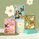 Three colorful greeting cards with animal designs on a green background with flower decorations.