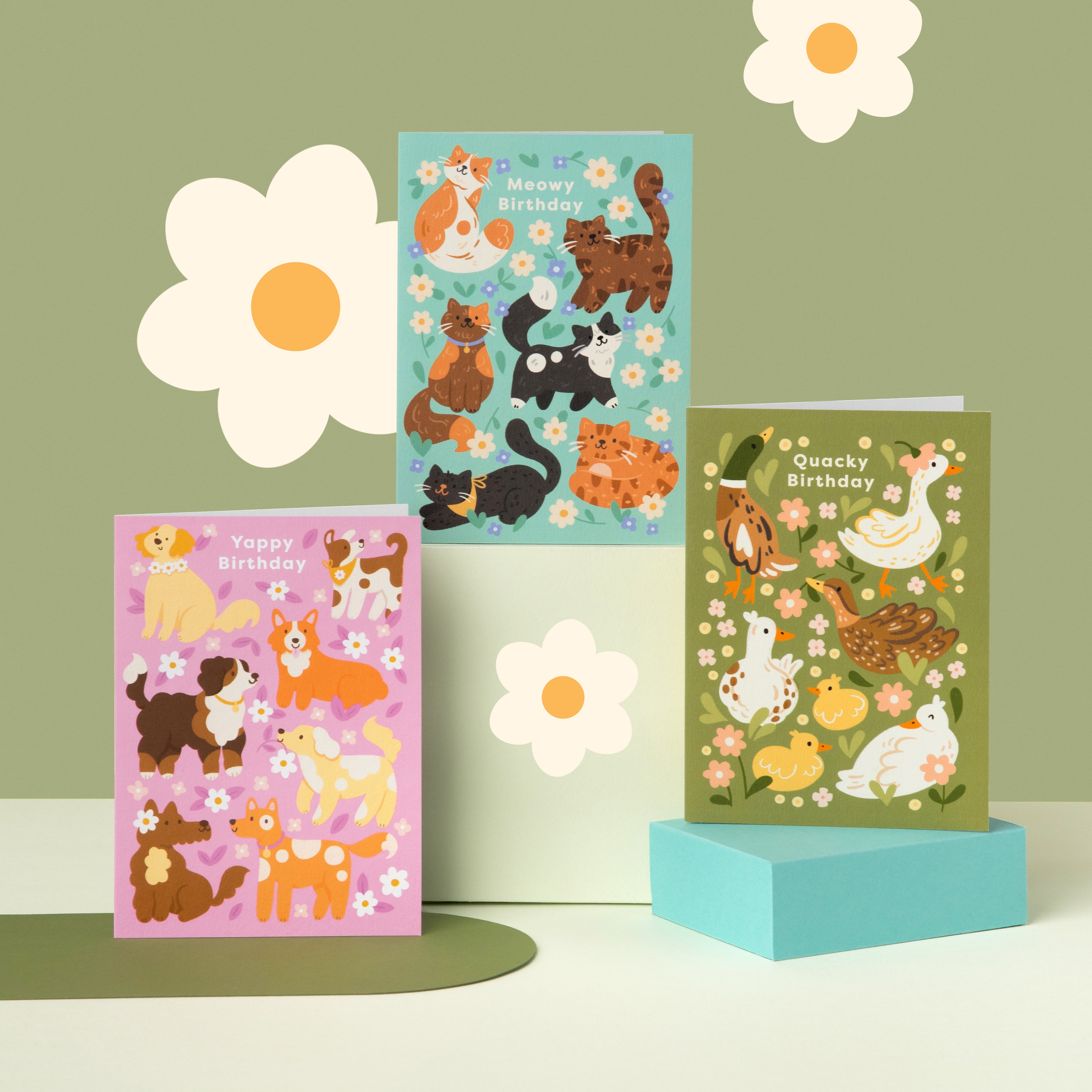 Three colorful greeting cards with animal designs on a green background with flower decorations.