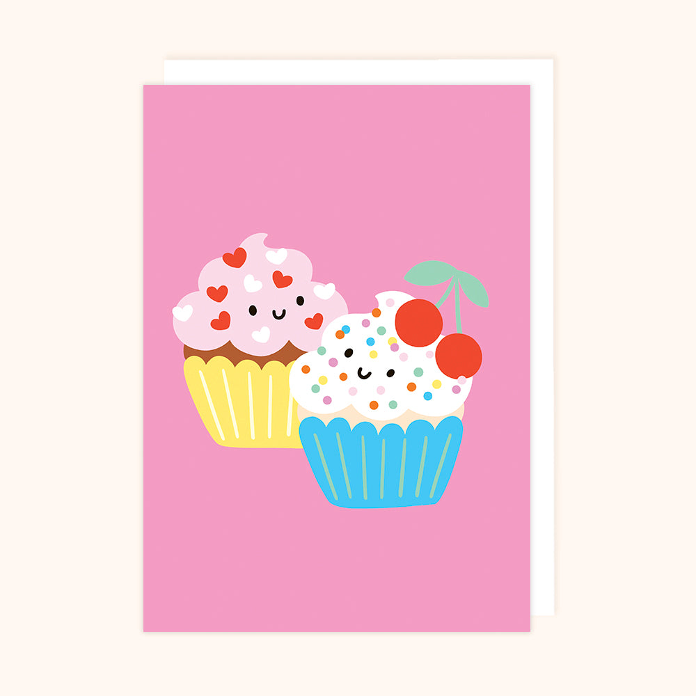 A colorful greetings card featuring two illustrated cupcakes with faces and cherries on a pink background.