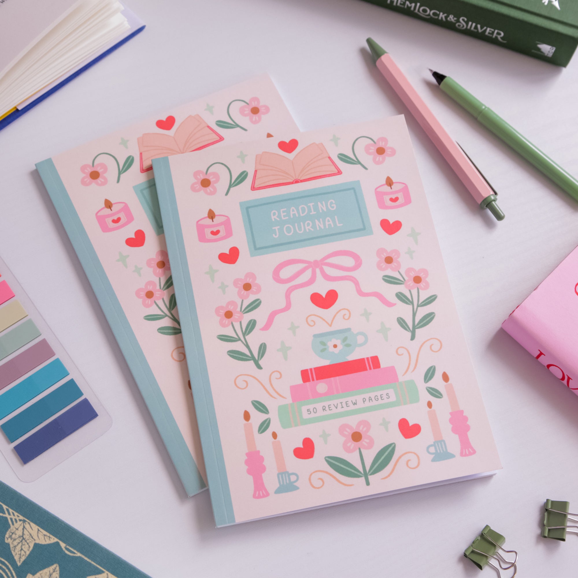Decorative journals with floral and book illustrations on a white surface with stationery items.