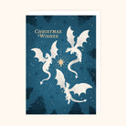 A Christmas greeting card featuring four white dragons flying around a glowing gold star on a dark blue background with silhouetted pine trees and the words 'Christmas Wishes' in gold.