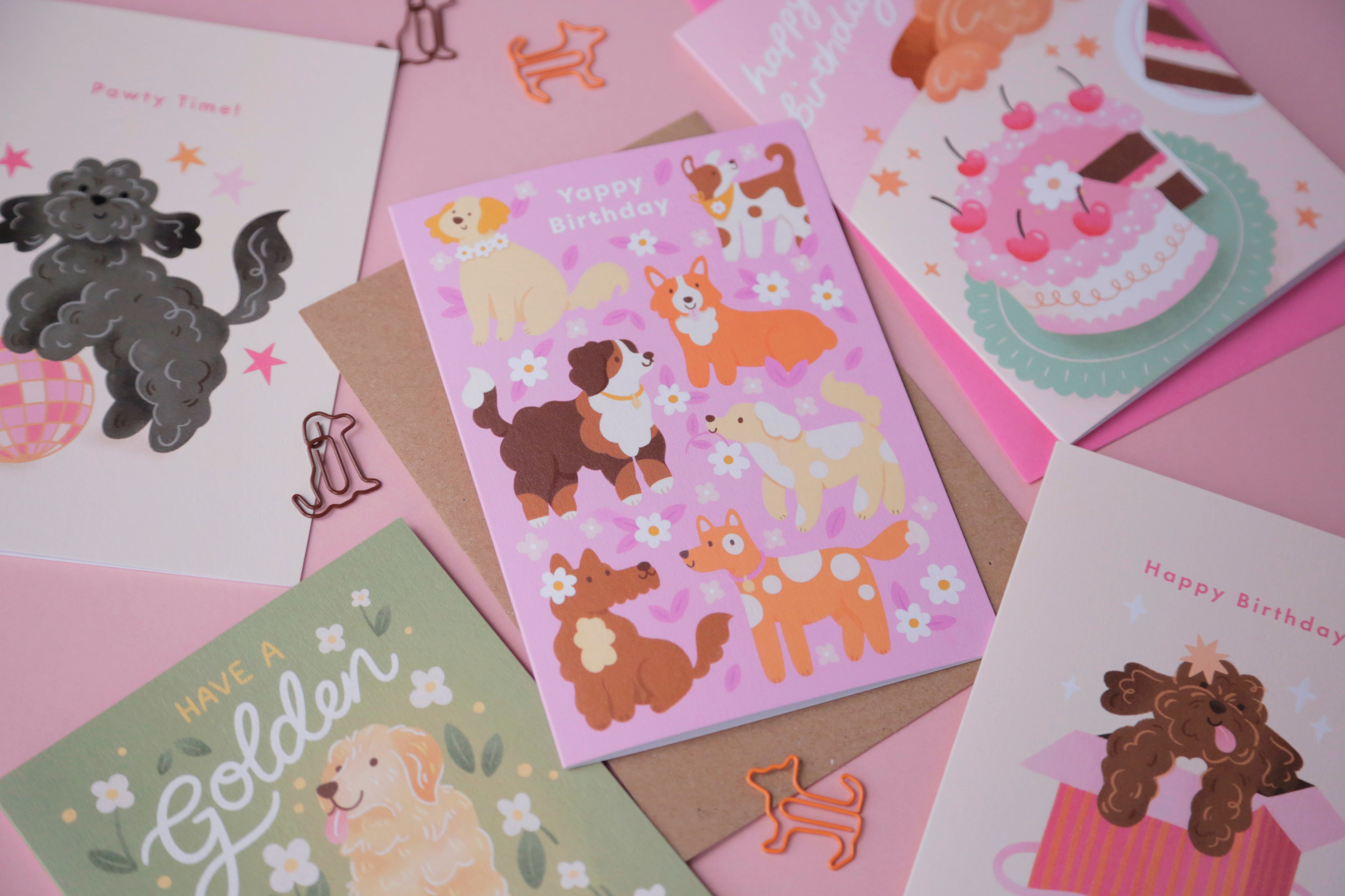 A photograph of a collection of dog-themed birthday cards on a pink background.